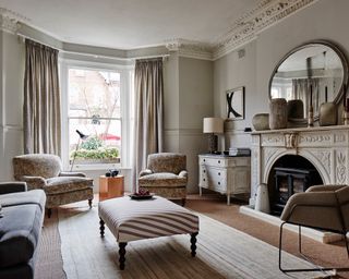 A neutral living room with pale paisley armchairs and large fireplace.