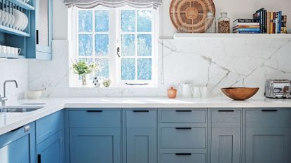 Pale blue kitchen cabinets with white walls abd veined marble backsplash plus open shelving and wooden decorative accents