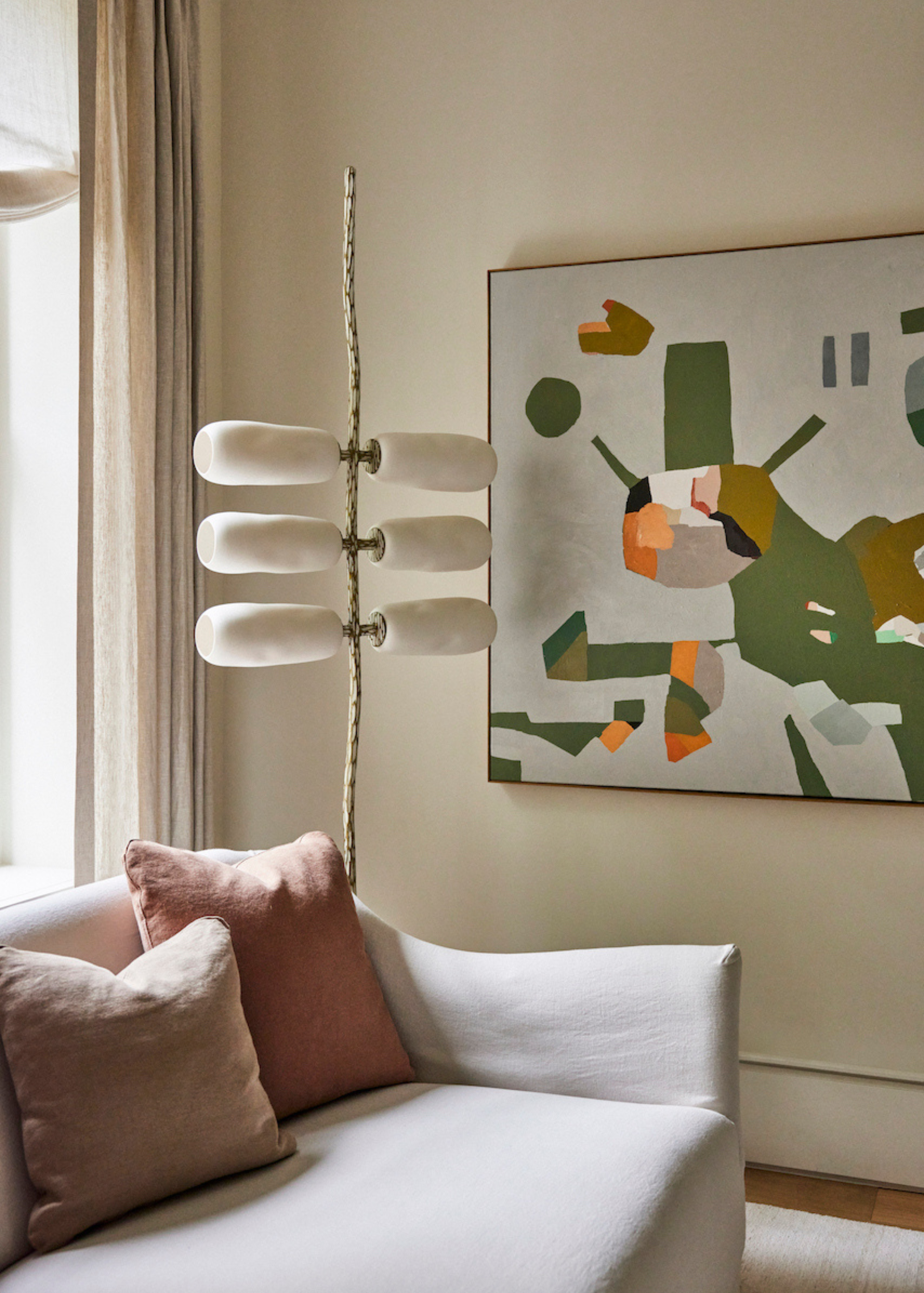 An off-white living room with a couch and colorful cushions near a standing lamp and wall art