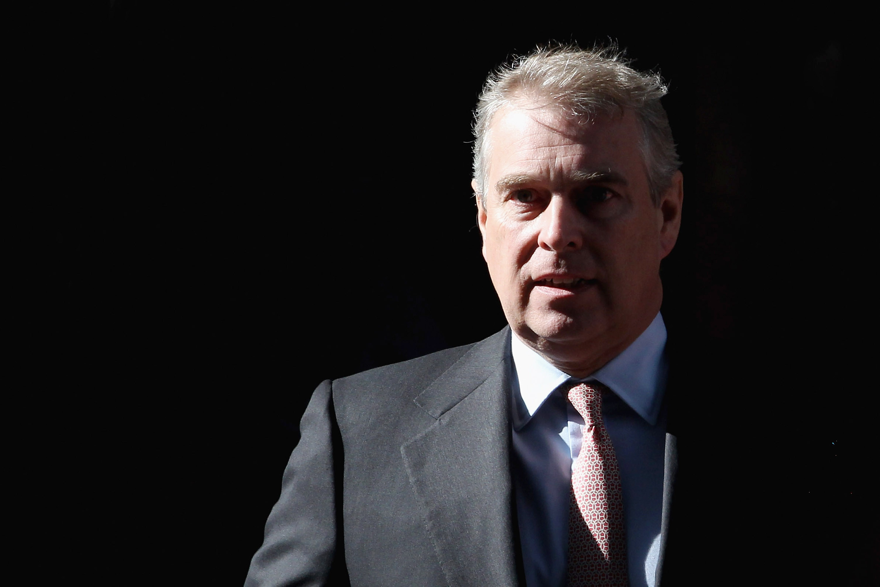 Prince Andrew wearing a suit standing in front of a black background