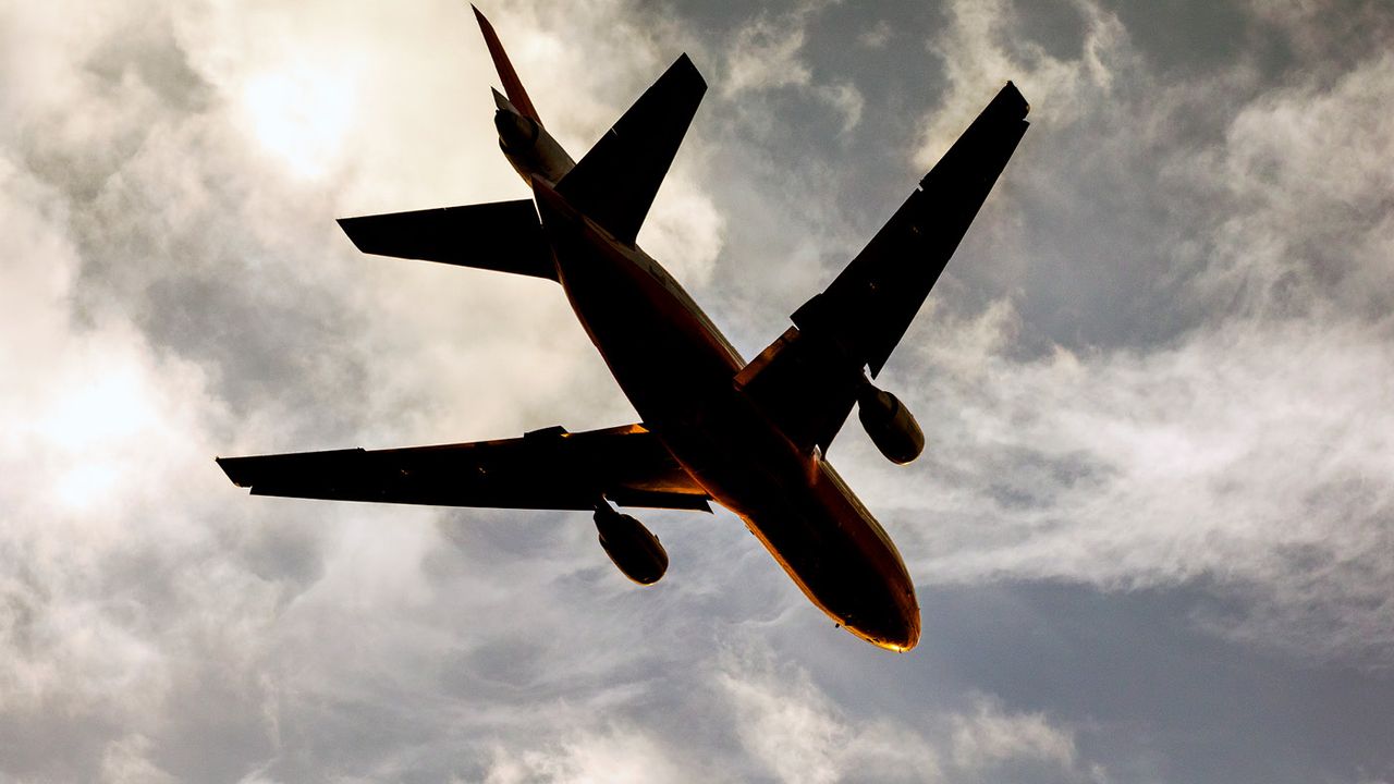 The underside of a plane landing in the evening against a cloudy sky