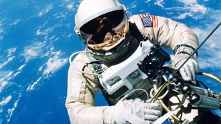 Astronaut Ed White floats in the microgravity of space outside the Gemini IV spacecraft. Behind him is the brilliant blue Earth and its white cloud cover. White is wearing a specially-designed space suit. The visor of the helmet is gold plated to protect him against the unfiltered rays of the sun. In his left hand is a Hand-Held Self-Maneuvering Unit with which he controls his movements in space.