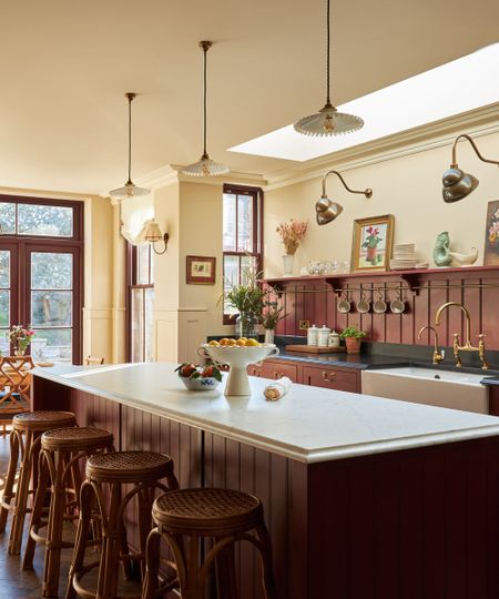 a large kitchen with oxblood red cabinets and paneled backsplash, black countertops, and warm neutral walls