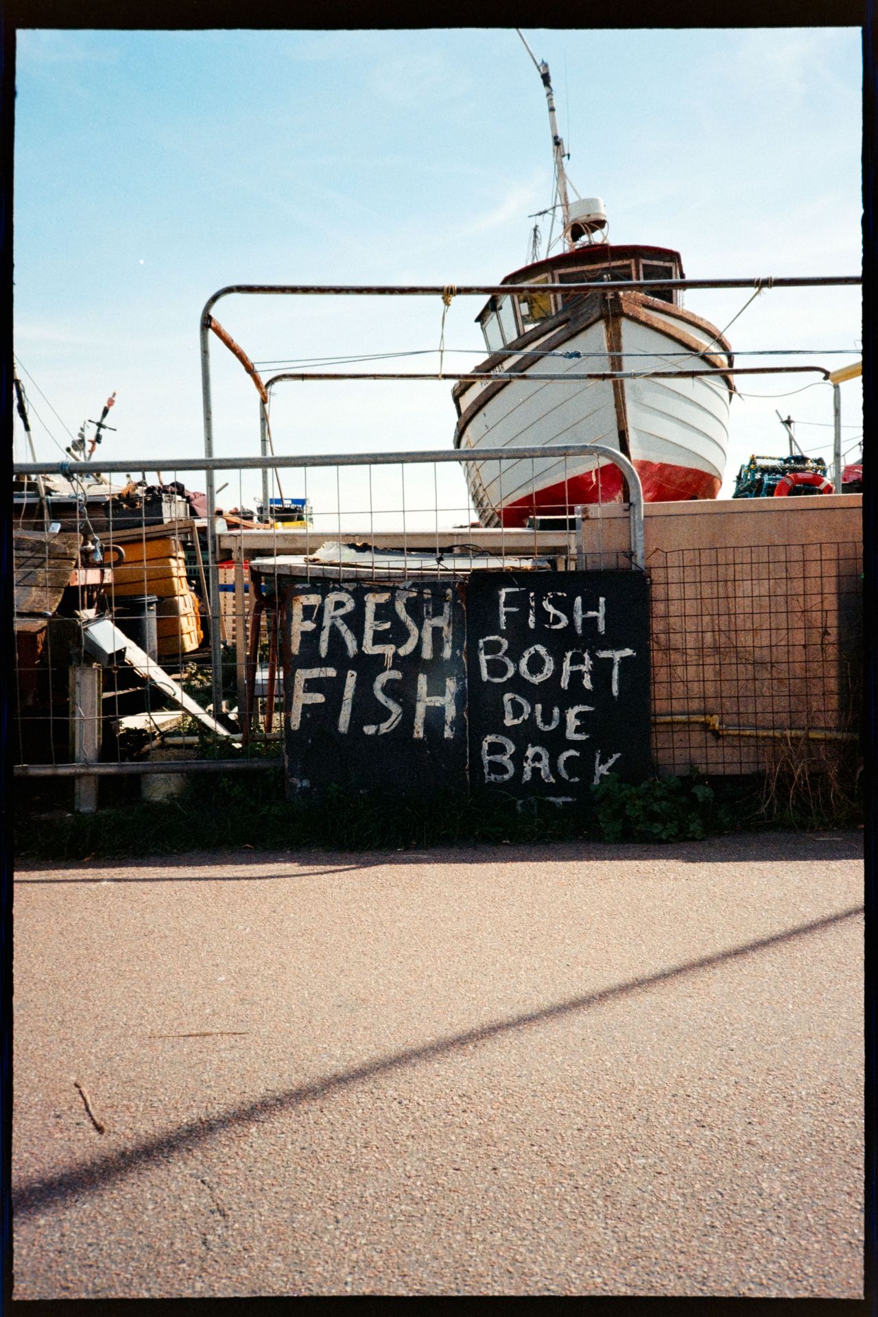 A fishing boat behind a fence with a hand-painted sign reading &ldquo;fresh fish, boat due back.&rdquo;