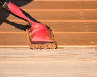 Staining a wooden deck with a staining pad.