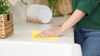 Woman cleaning kitchen countertop with a yellow cloth