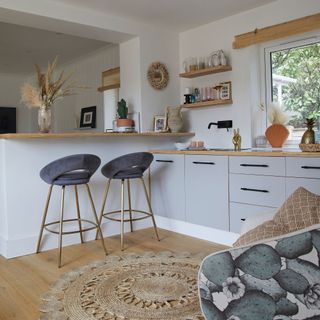 white kitchen breakfast bar with bar stools round rug wood worktops grey cabinets shell vase rattan blinds