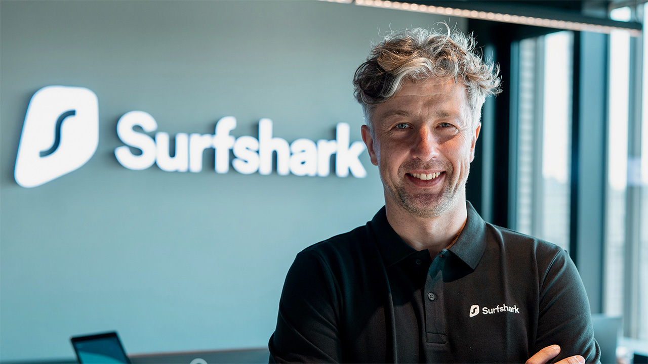 Headshot of Vytautas Kaziukonis, Surfshark CEO, with a neon Surfshark logo in the background.