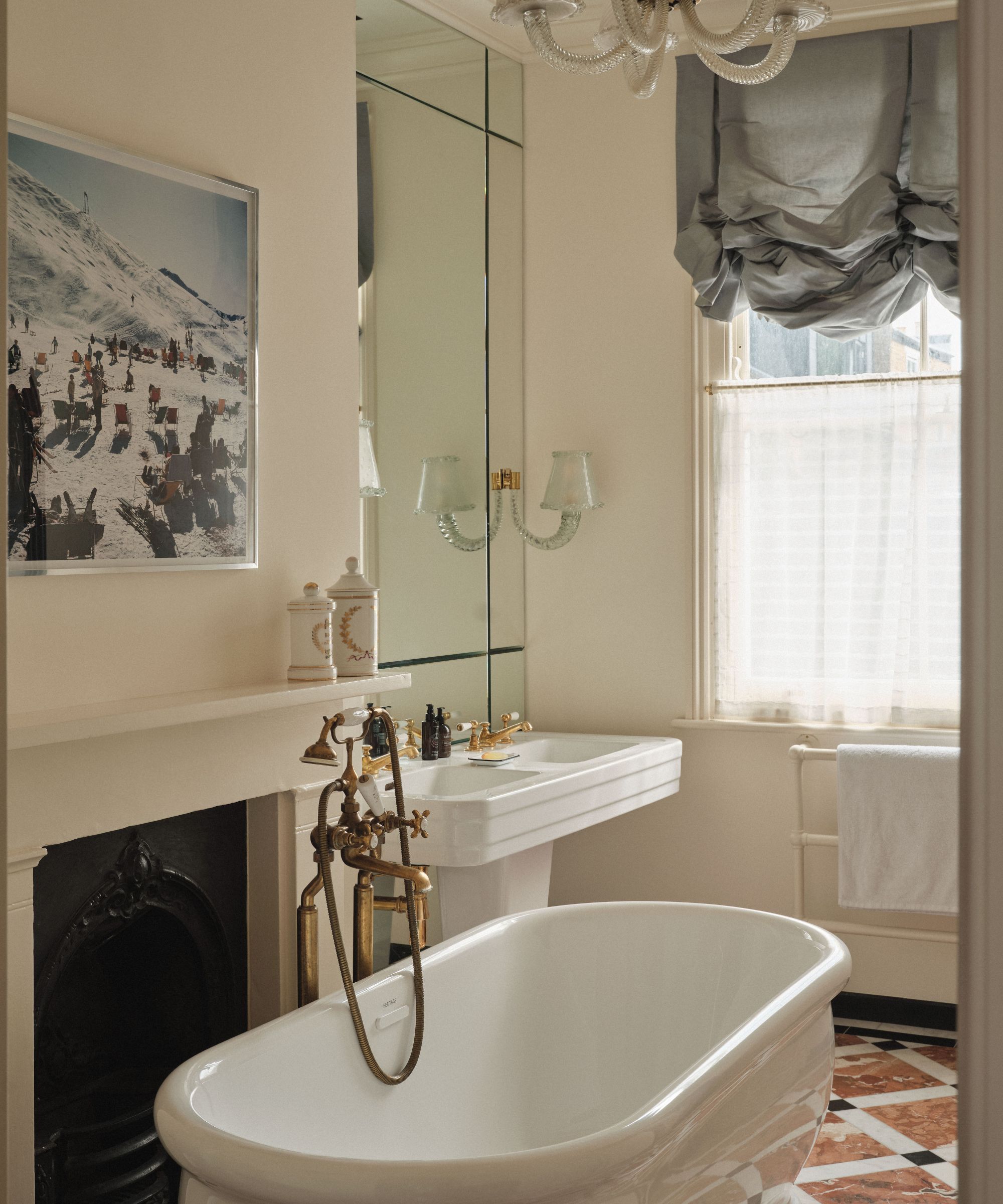 Romantic bathroom with a silk Austrian blind, large fireplace with ski photograph above, footed bath and gold tap