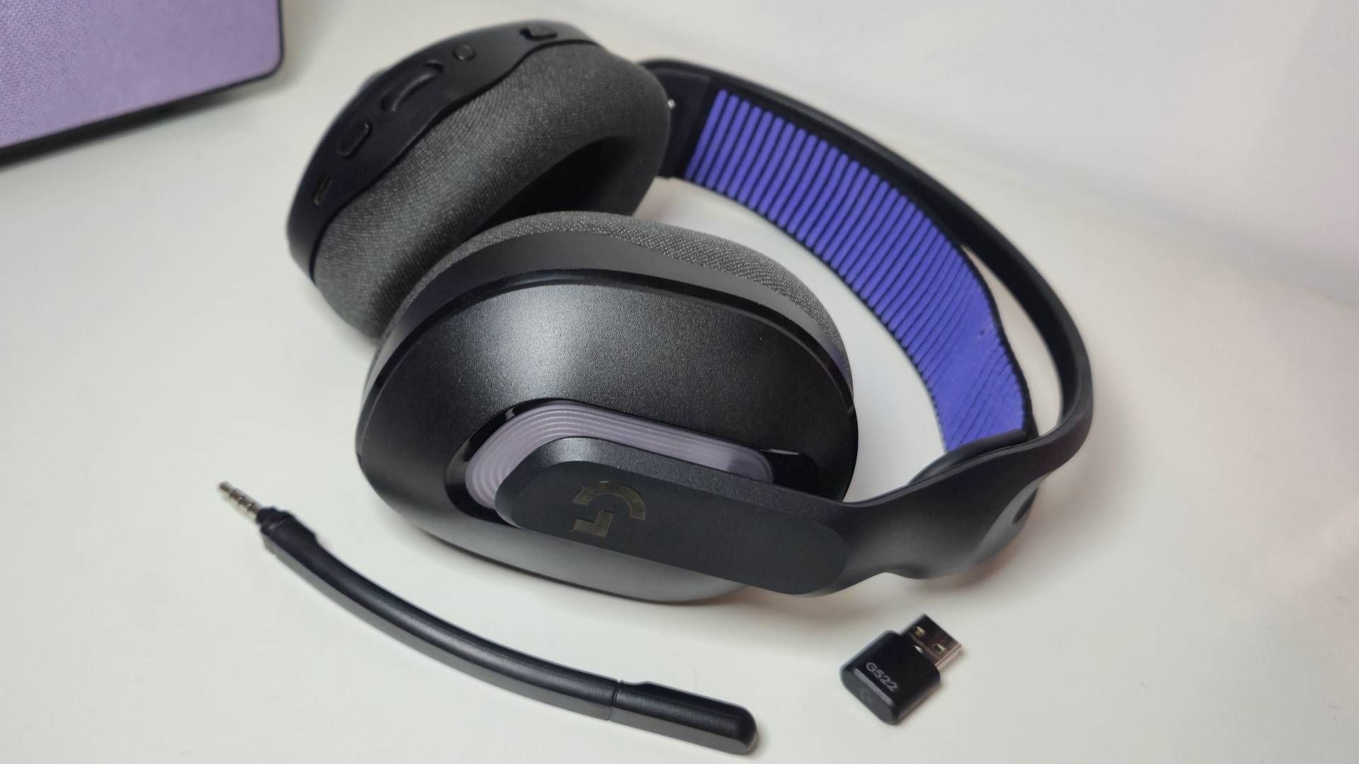Photo by Rosalie Newcombe of the Logitech G522 Lightspeed headset sitting on a white desk with its microphone and 2.4GHz dongle next to it.