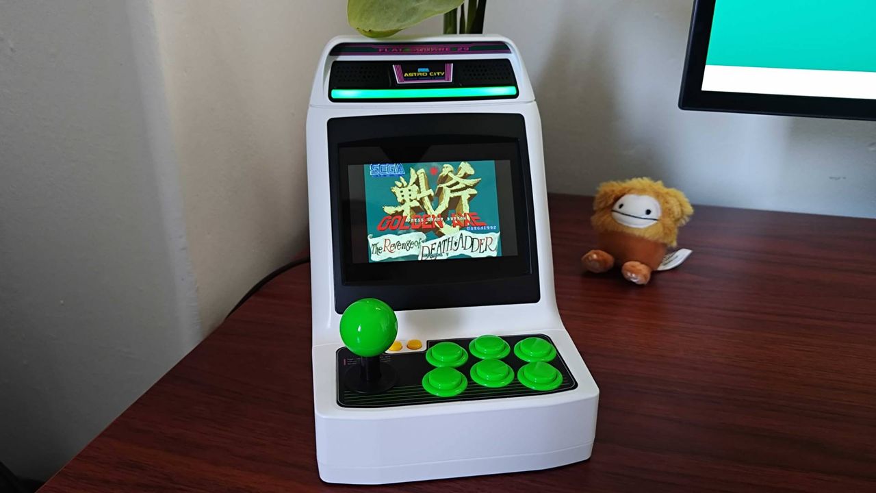 Sega Astro City Mini on woodgrain desk facing forward with Golden Axe: The Revenge of Death Adder title on screen.