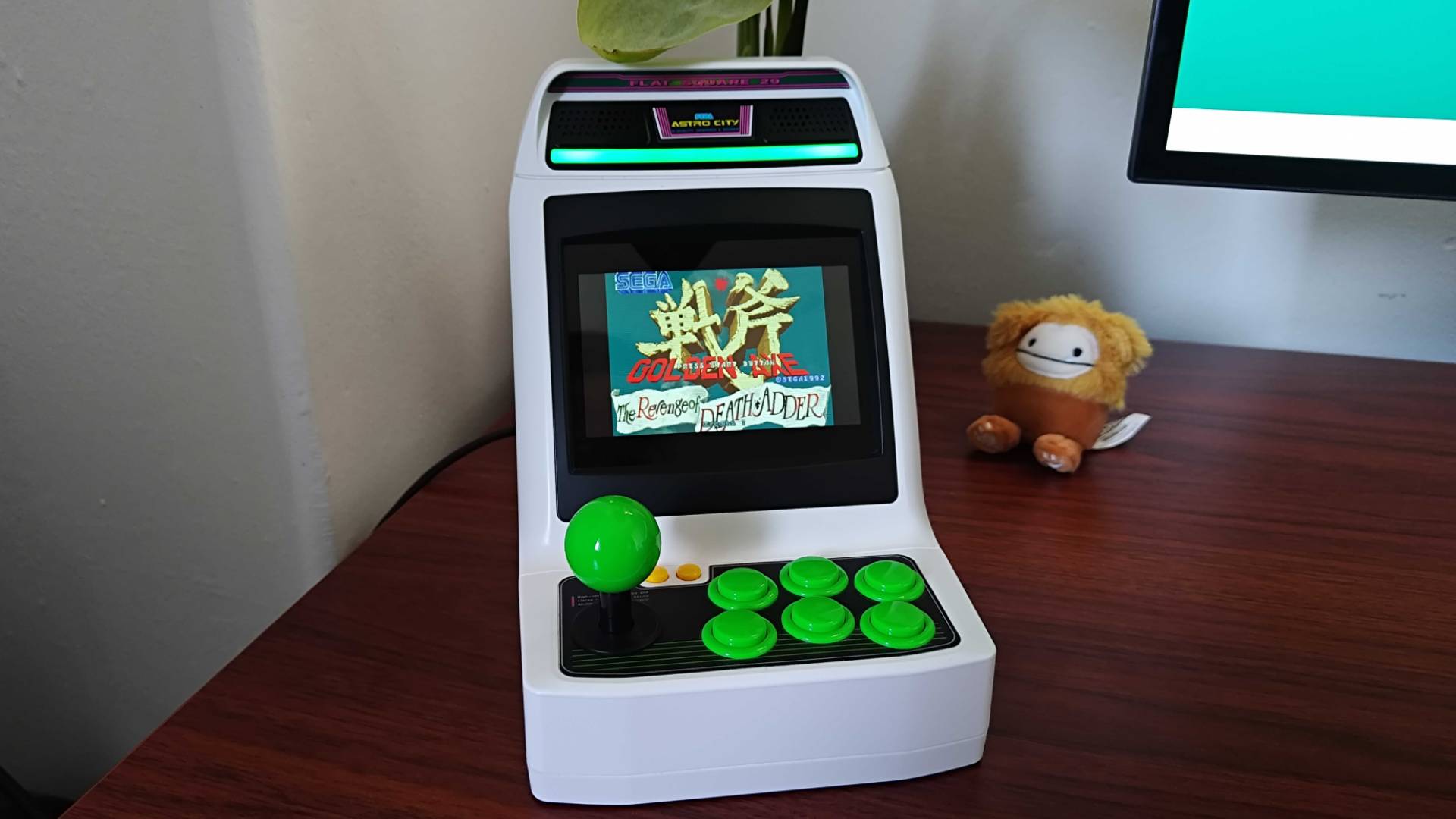 Sega Astro City Mini on woodgrain desk facing forward with Golden Axe: The Revenge of Death Adder title on screen.