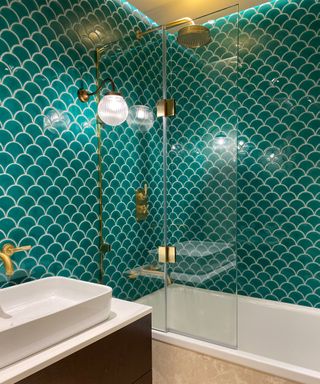 Modern bathroom with green scalloped wall tiles, brass fixtures and fittings, elegant wall light with bras fixture and glass diffuser, strip ceiling lighting above shower