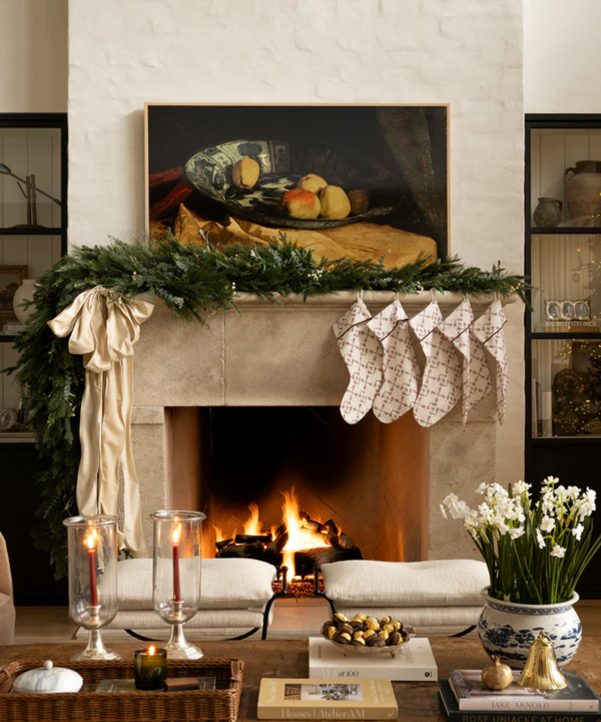 a Christmas mantel decorated with asymmetrical garland, a large white bow, and five stockings on one end