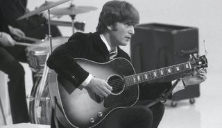 John Lennon holds an acoustic guitar while filming The Beatles' 'Hard Day's Night' movie at the Scala Theatre