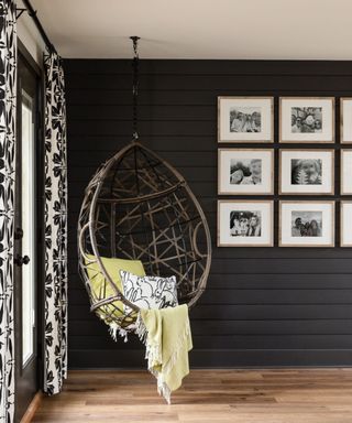 family photos in a grid style gallery wall against a black panelled wall with a hanging rattan egg chair