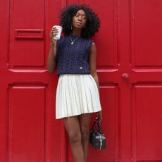 a photo of a woman wearing one a white pleated mini skirt with a blue sweater vest at the start of a roundup of the best pleated mini skirts