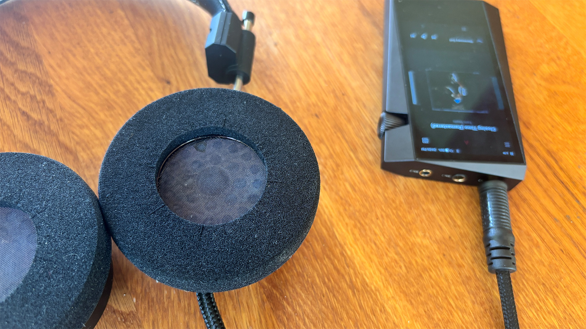 Grado SR325 Classic over-ear headphones on wooden desk plugged into music player, detail of foam inner ear-cups