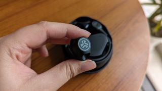 JLab Work Buds wireless earbuds with detachable microphone held in hand while the case is kept on a table.