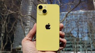 En hand håller upp en Apple iPhone 14 i en gul färg.