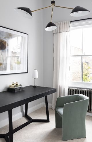 home office with black desk, green armchair, table lamp, retro pendant light, radiator, gray walls, artwork, drapes, carpet
