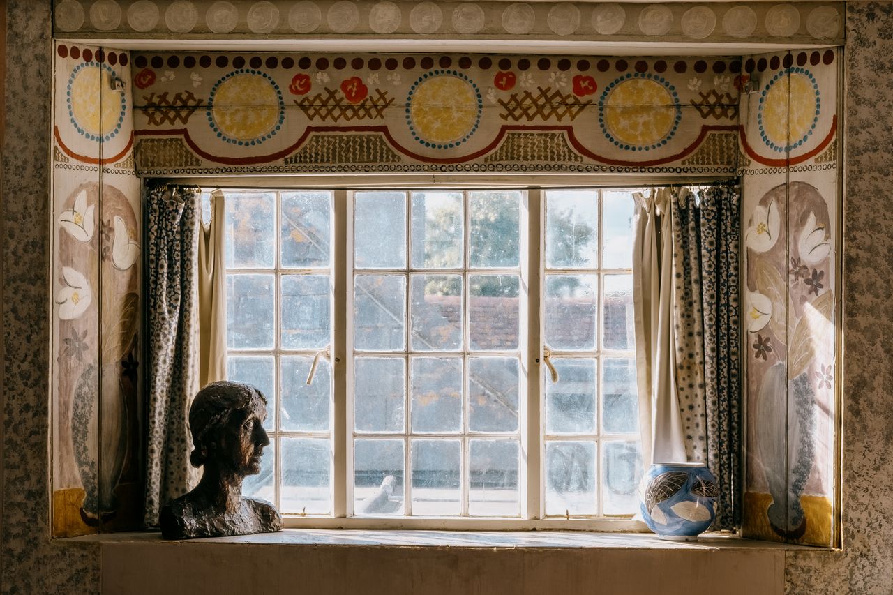 A murals-covered study features whimsical abstract and figurative painted motifs, handcrafted ceramics, colorful curtains, and a bronze bust of a woman.