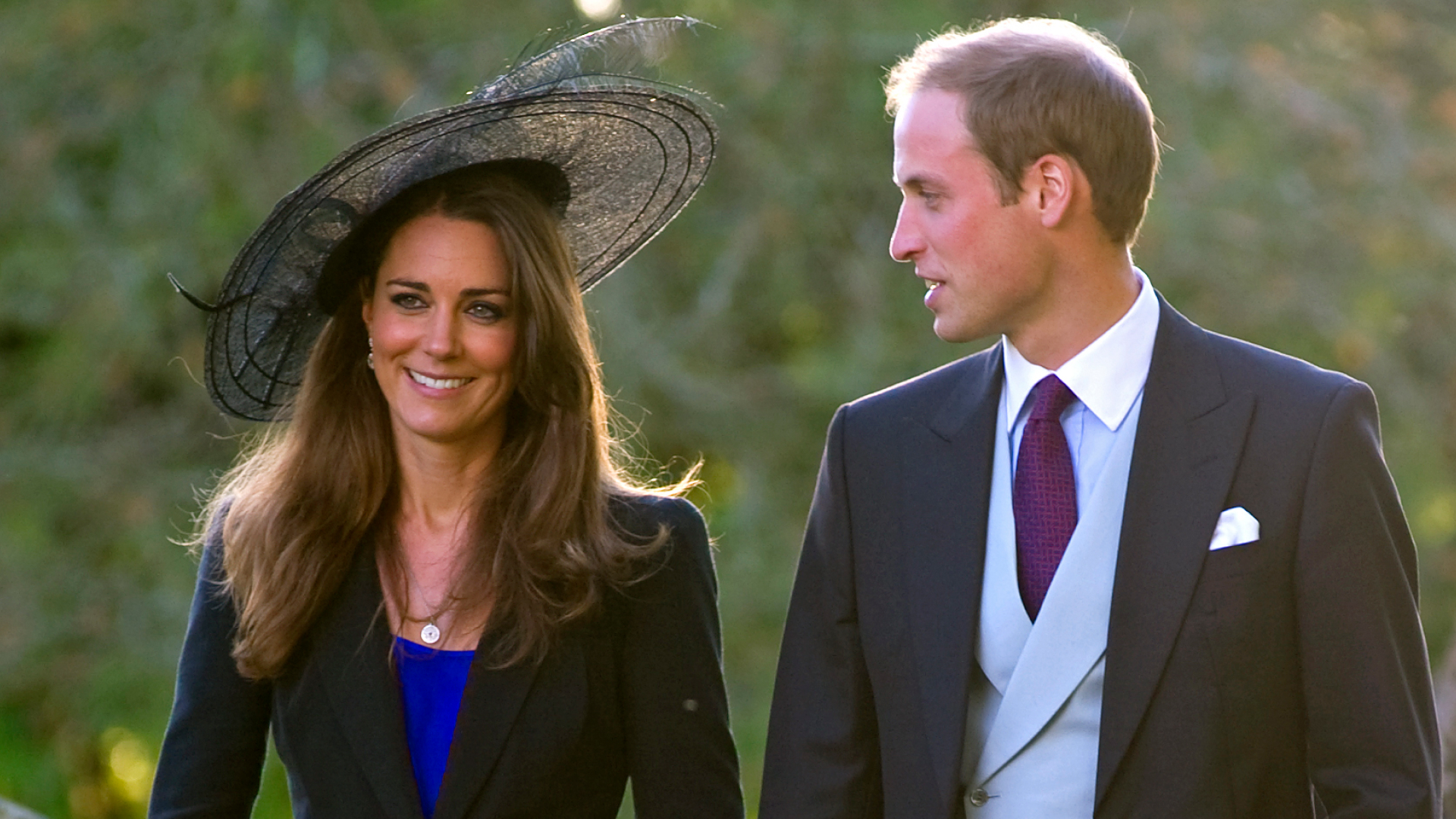 Kate Middleton wears a royal blue dress and a black jacket and hat while attending a wedding with Prince William in October 2010