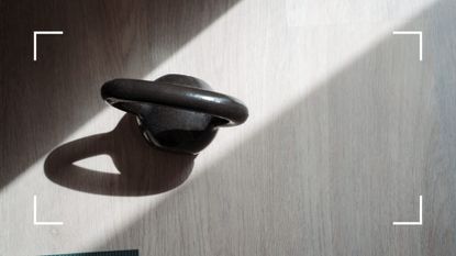 Kettlebell sitting on wooden floor with sunbeam over it, representing the difference between dumbbells vs kettlebells