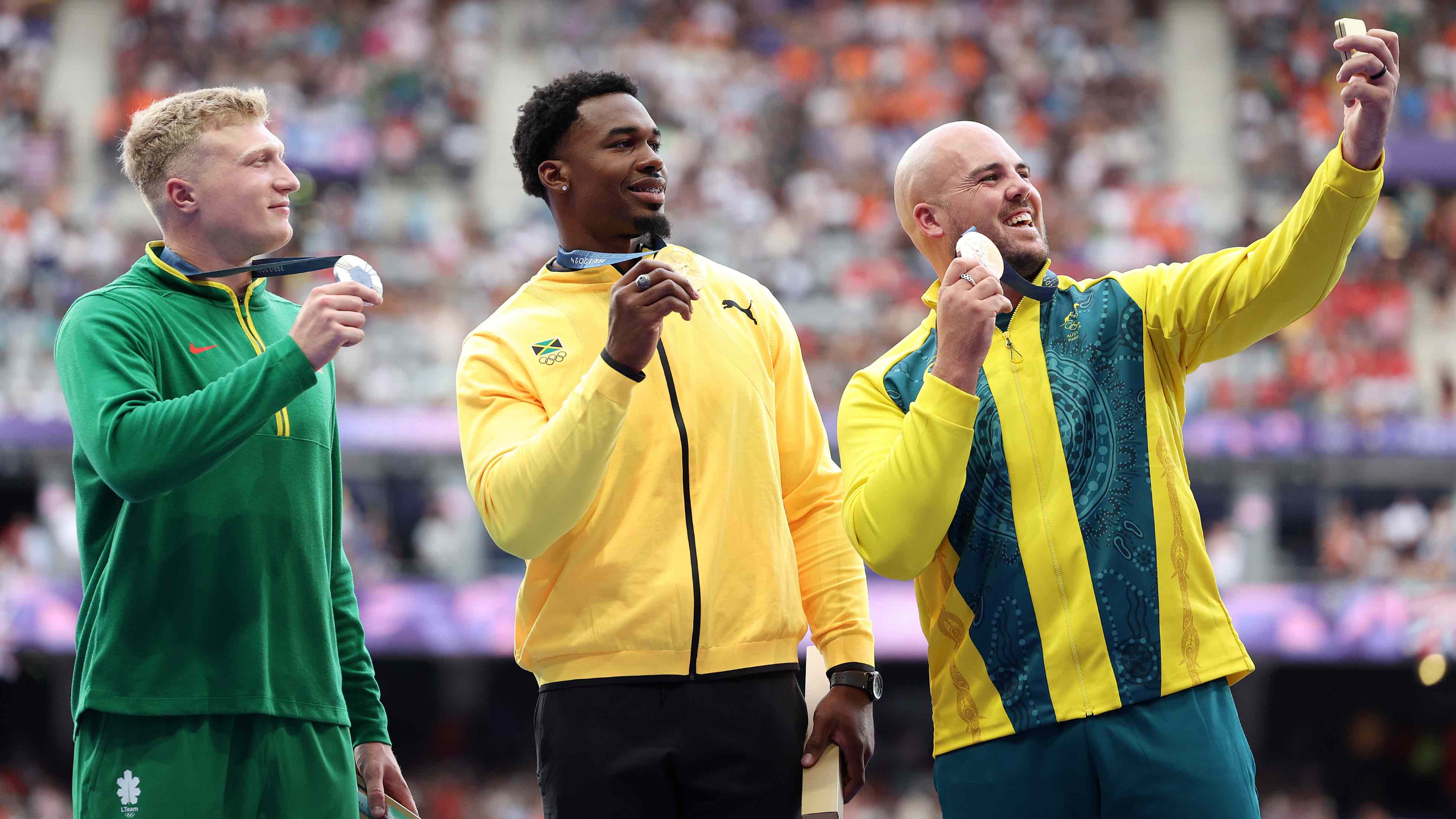 Gold medalists Roje Stona of Team Jamaica (C), silver medalists Mykolas Alekna of Team Lithuania (L) and Matthew Denny of Team Australia (R) take a victory selfie with the Samsung Galaxy Z Flip6 Olympic Edition on the podium during the Men's Discus Throw medal ceremony on day thirteen of the Paris 2024 Olympic Games at Stade de France on August 8, 2024 in France. (Photo by Elsa/Getty Images)