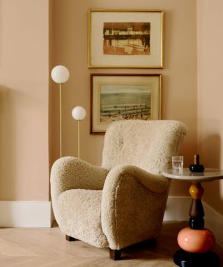 boucle, curved armchair in a corner with two framed artprints and a gold floor standing modern floor lamp