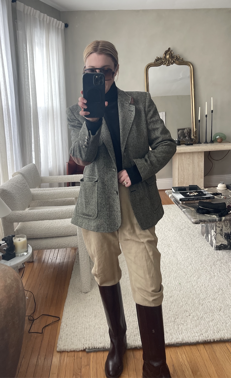 wearing a gray blazer, black, turtleneck sweater, tan pants, and brown boots