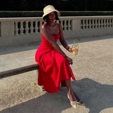 Woman wears red dress, white shoes, woven hat