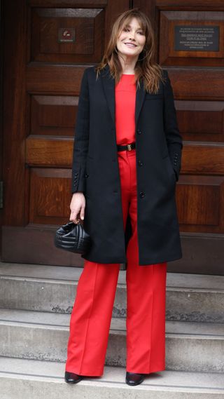 Carla Bruni red trousers black coat