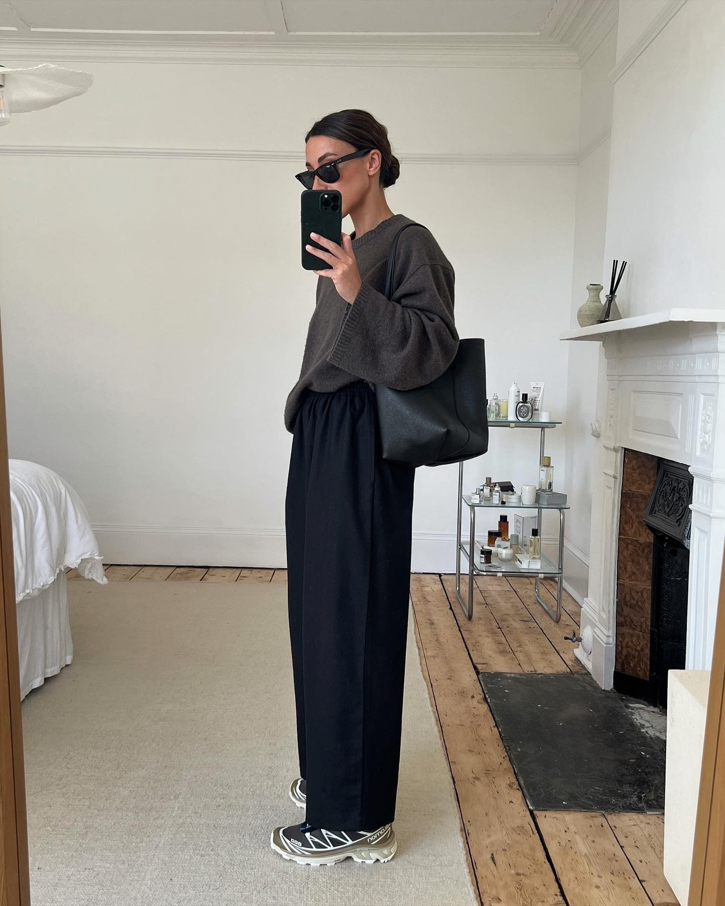 Influencer wears Salomon sneakers with black trousers and an oversize brown sweater.