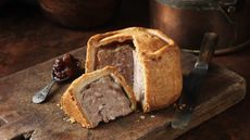 Pork pie on wooden board with spoonful of chutney and knife