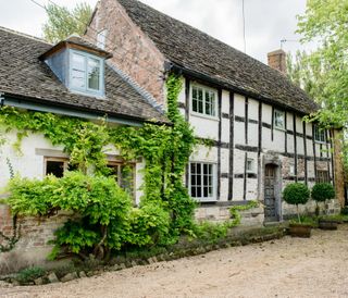 Elizabethan timbered cottage with wisteria growing up it and a gravel drive. Work studio of milliner Jessie Clifford at Frampton Court, a Palladian 18th century home in the Cotswolds and the Elizabeth cottage that she shares with husband Harry Spurr and their family.