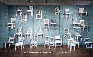 White-painted wooden chairs suspended across a blue-tiled wall