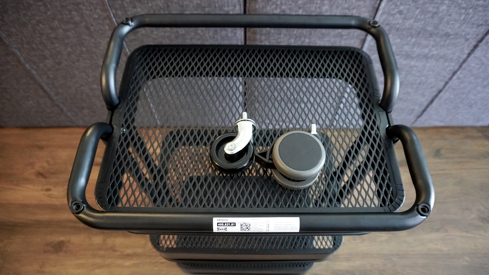 An IKEA R&amp;Aring;SKOG utility cart upside down with its stock casters next to a pair of Soft Roll Desk Casters from Uplift Desk