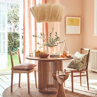 A dining room with a round table and pink walls, paired with striped red and white curtains and a ruffled pendant light above