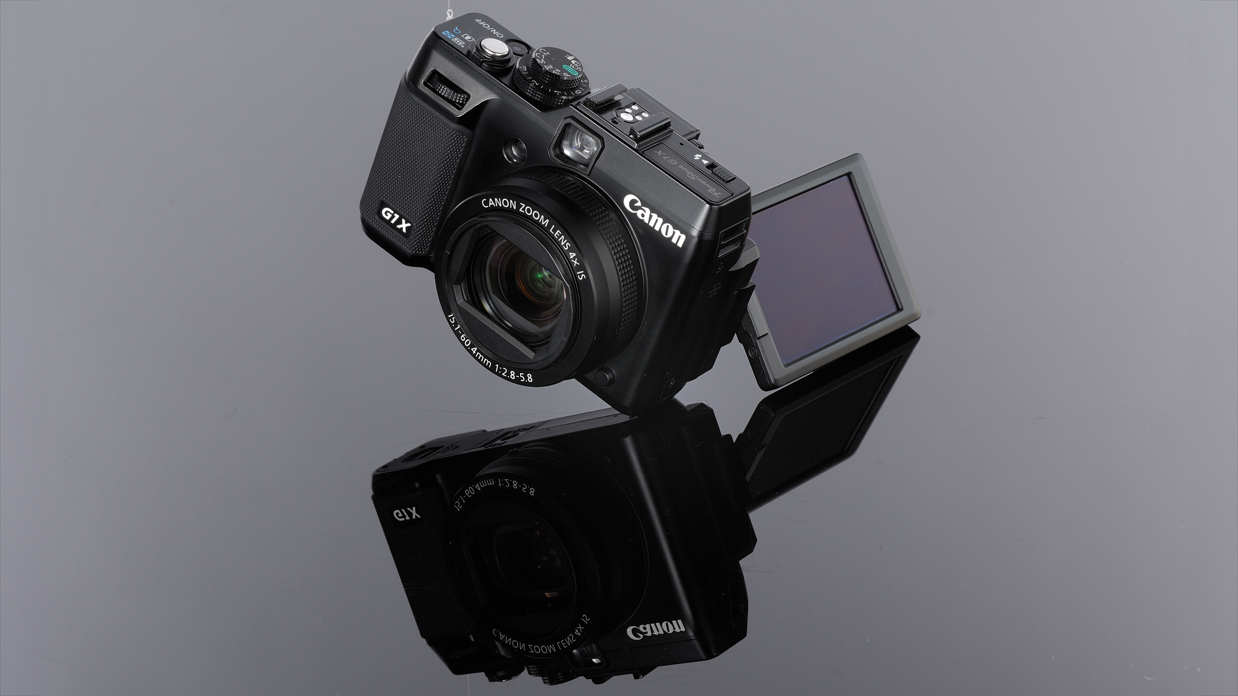 Black Canon G1X camera with flip-out LCD screen, reflected on a glossy black surface