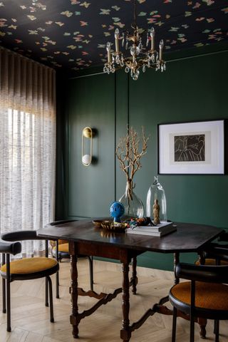 A dining room with green walls and wallpapered ceiling