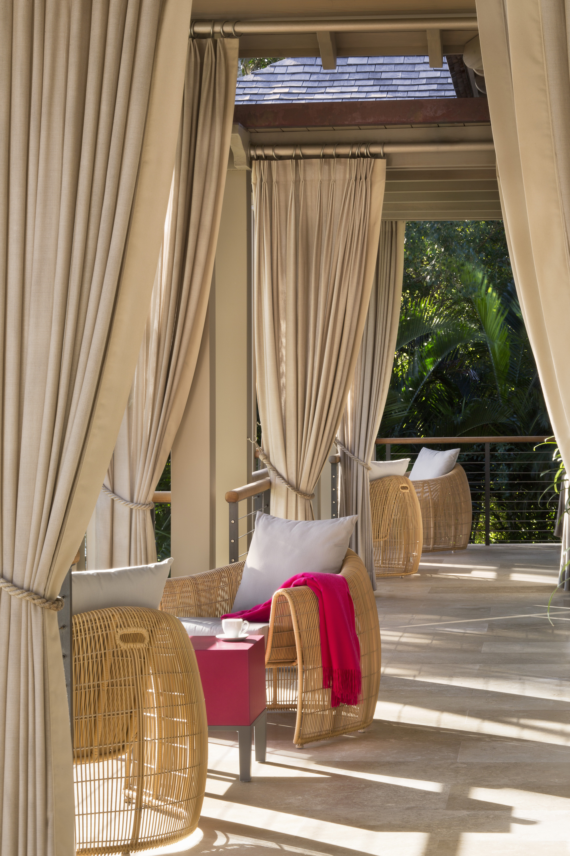 An outdoor terrace with beige curtains hanging next to every column tied back with rope
