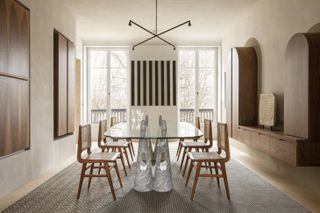 Apartment XVIII by Studio Razavi Architecture - a large glass table with six wood chairs; two floor to ceiling balcony doorways. An X shaped hanging light fixture.