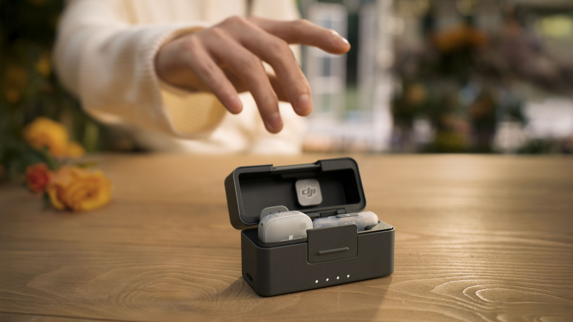 DJI Mic Mini 2 charging case and a person's hand is reaching out to pick it up