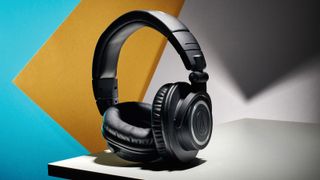 A pair of Audio-Technica studio headphones on a coloured background