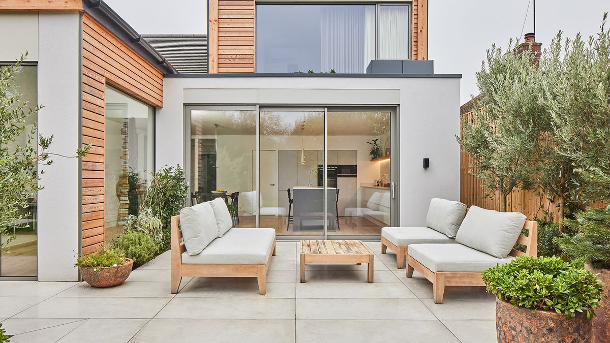 A light patio in front of a contemporary home with glass sliding doors and patio furniture