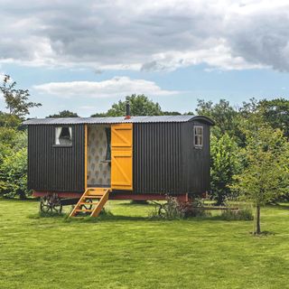 Raised black shepherd's hut in garden on lawn next to tree