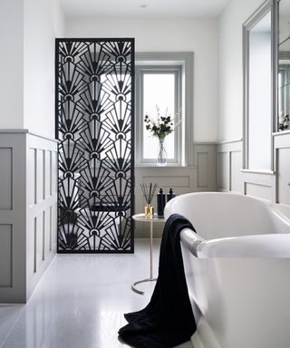 An example of ensuite ideas showing an ensuite with a black art deco panel and a white bath