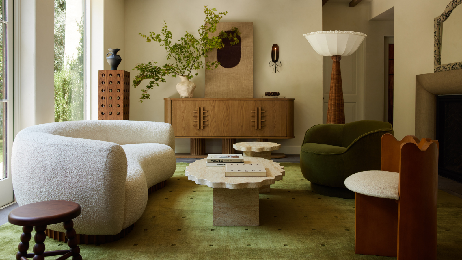 a warm and inviting living room with a large green area rug, a white boucle couch, mismatched accent chairs, a marble coffee table, and a large wood sideboard in the back adjacent to a rattan floor lamp