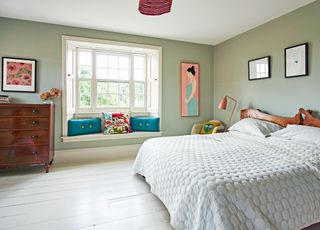 bedroom with pale green walls rustic wooden bedhead and coral colored lamp and picture